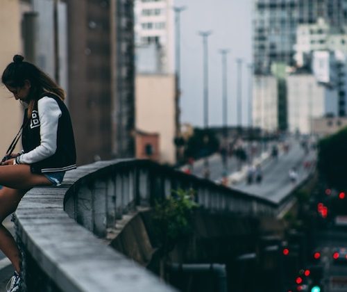 a girl sitting on a bridge in the city