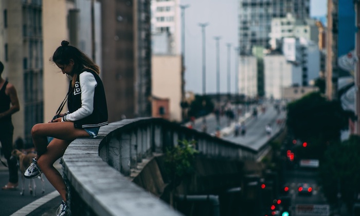 a girl sitting on a bridge in the city