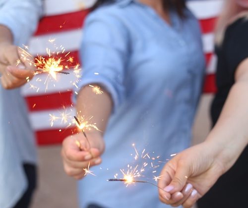 girls holding sparklers in front of american flag