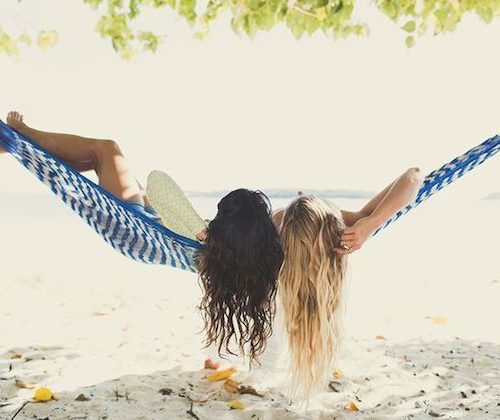 two girls lying in a hammock on the beach