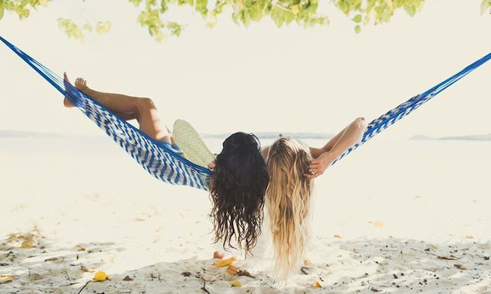 two girls lying in a hammock on the beach