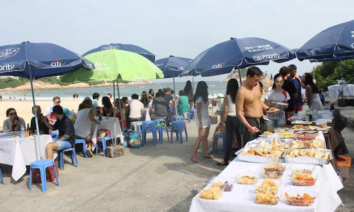 people eating from a buffet on the beach 