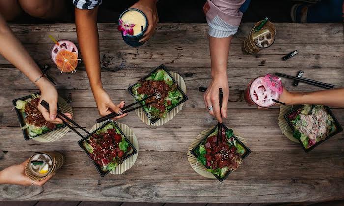 group of friends sharing cocktails and poke bowls