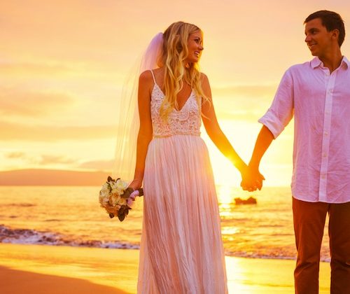 a newly wed couple on the beach at sunset