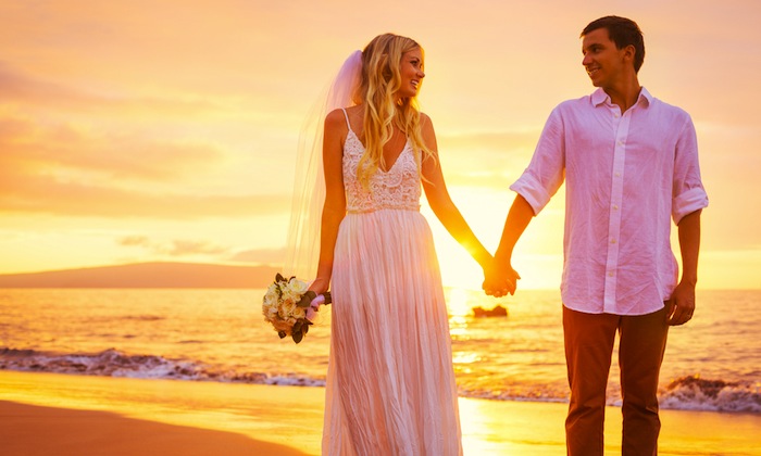 a newly wed couple on the beach at sunset