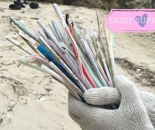 a pair of gloves holding straws on the beach