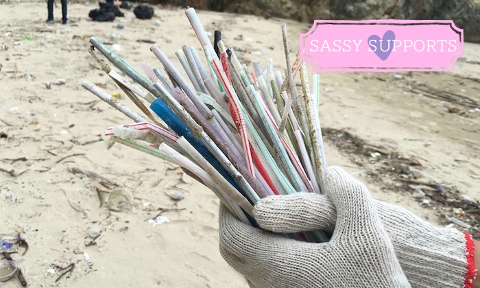 a pair of gloves holding straws on the beach