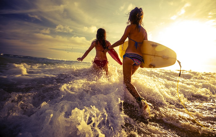 two girls running into waves with surfboards