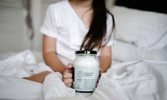girl sitting in bed with a jar of coconut oil