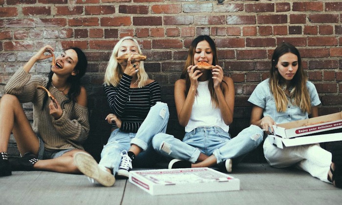friends sitting against a wall eating pizza