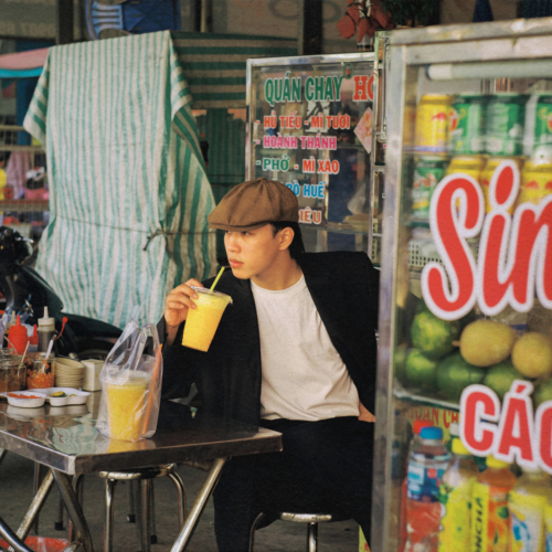 asian man sitting at a cafe in chiang mai, thailand drinking a mango smoothie during summer