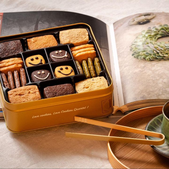 Open gift box showing seven cookie types set beside open coffee table photo book with tea service.