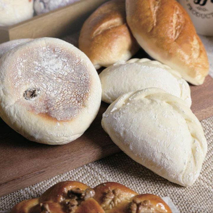 Variety of four pastries on wooden board and woven placemat, with porcelain ingredients canisters on stone table.