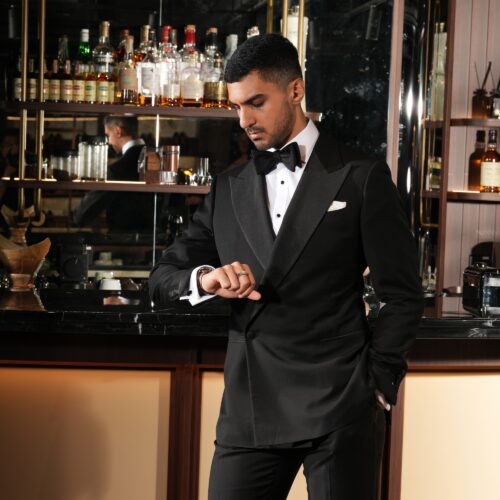 man in a custom black wedding suit with a bowtie in front of a bar at his wedding