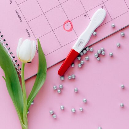 A close-up of a pregnancy test, calendar, and tulip arranged on a pink surface, representing egg freezing procedures in hong kong.